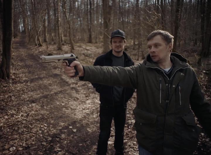 Oleg holding a gun in the forest, Andrzej on the background