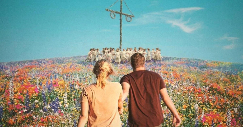 A couple in a field of flowers, against a blue sky, the may pole ahead of them