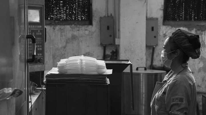 A woman, in a factory, in front of a pile of plastic spoons